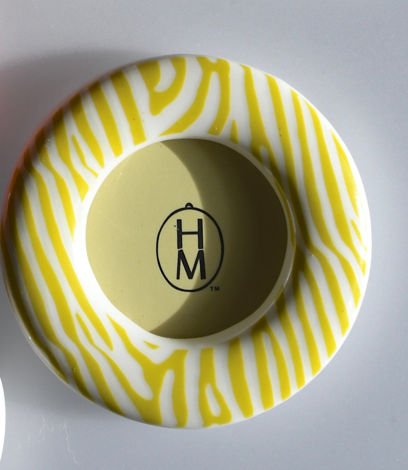 Round ceramic frame with yellow and white pattern and 'H M' logo on a gray background