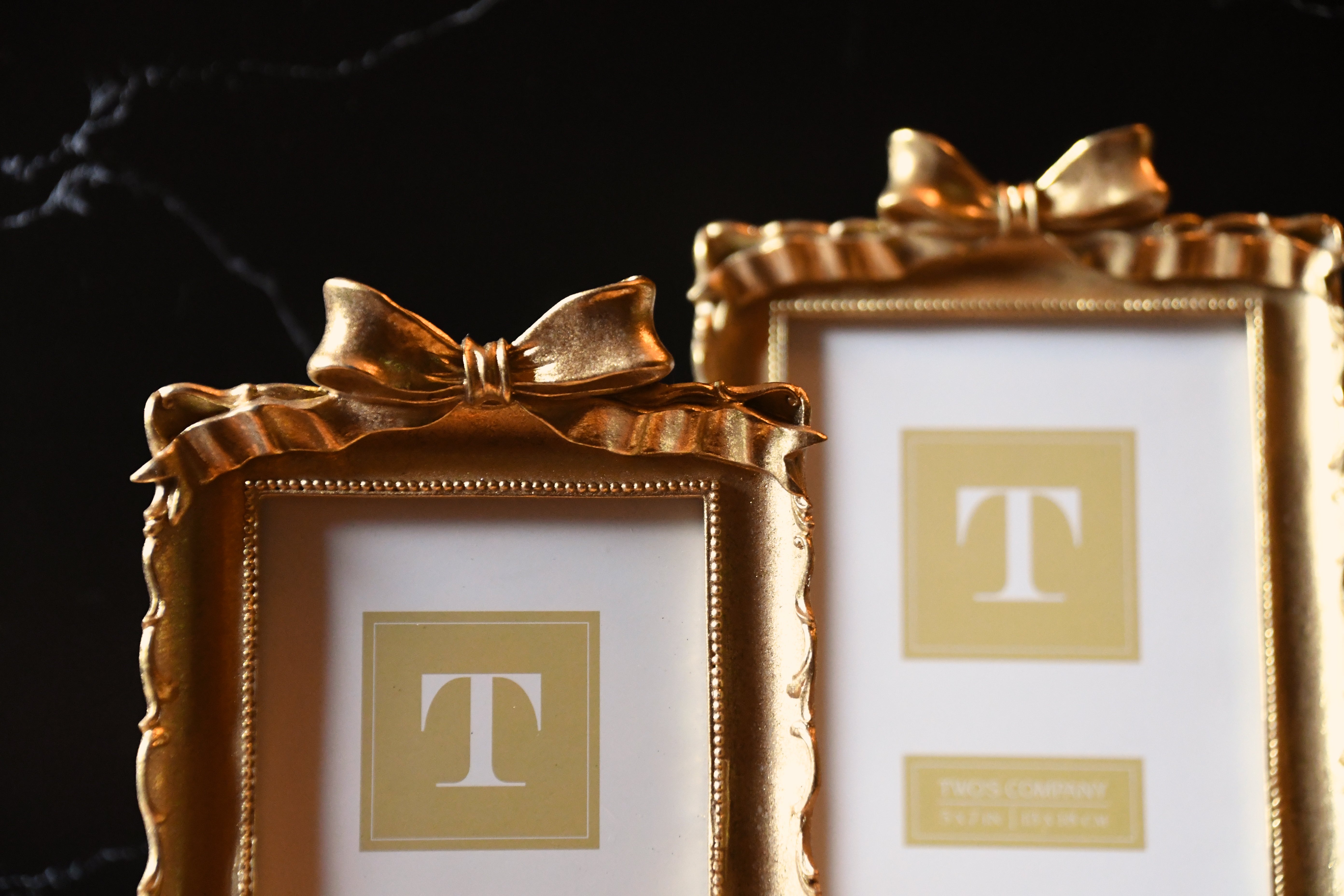 Two gold picture frames with decorative bows on a black background