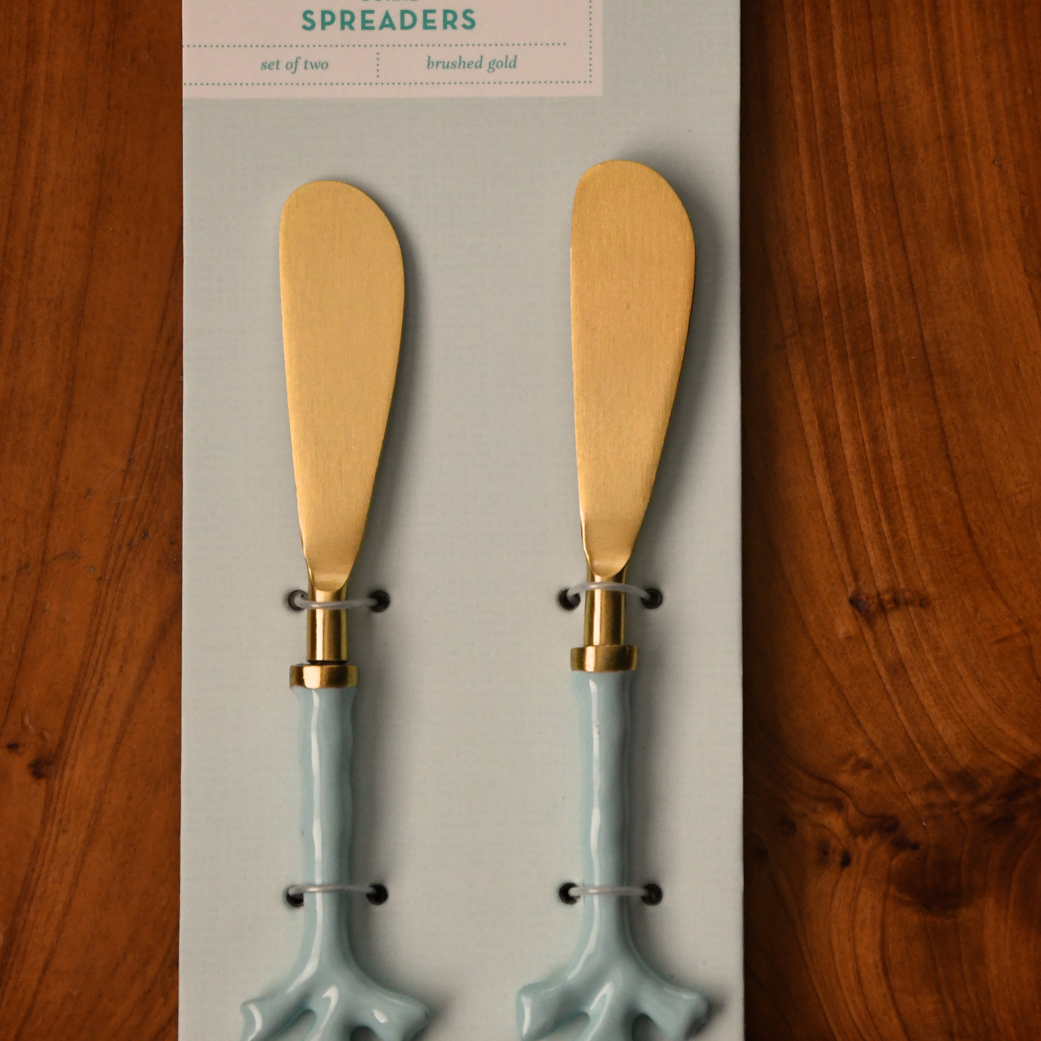 Two coral spreaders on a Two's Company branded card against a wooden background