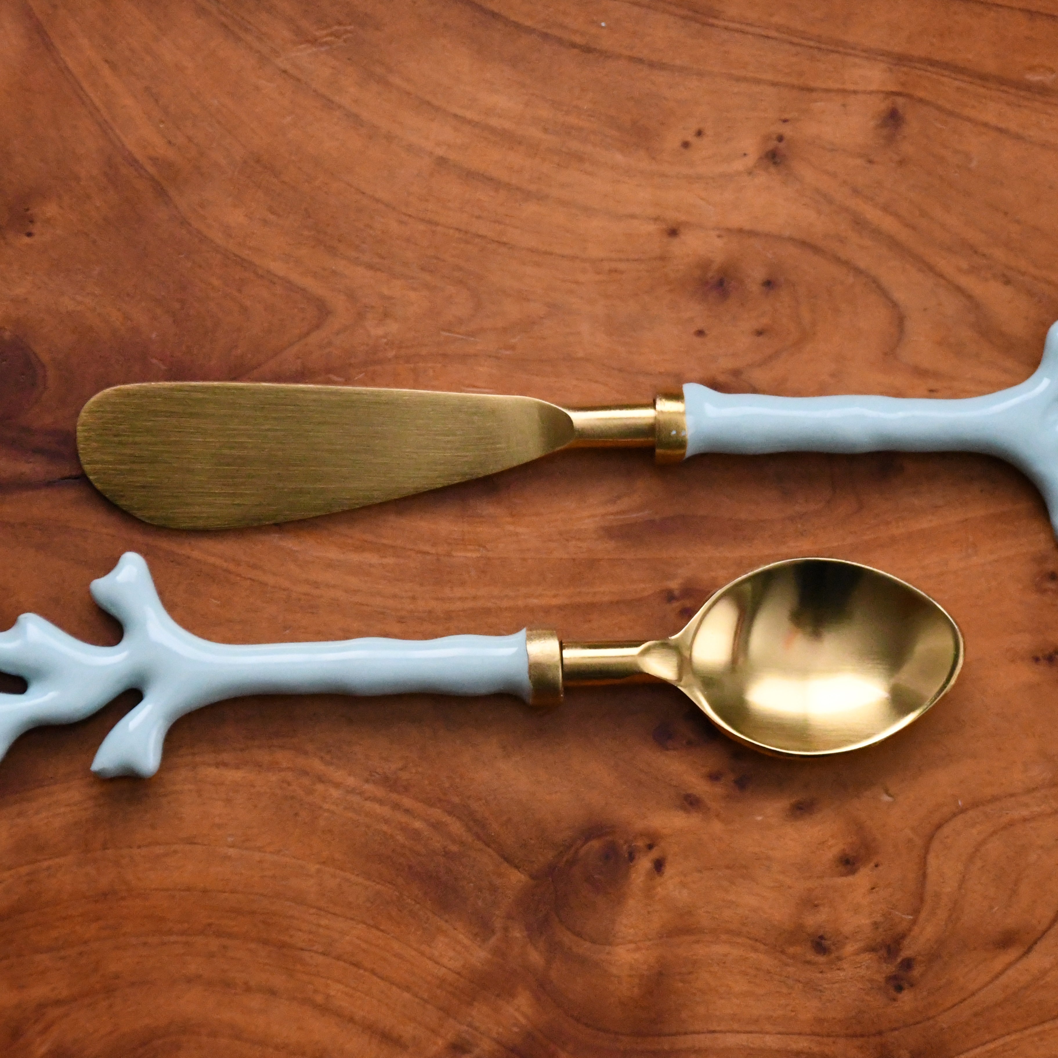 Gold spoon and butter knife with white coral-like handles on a wooden surface