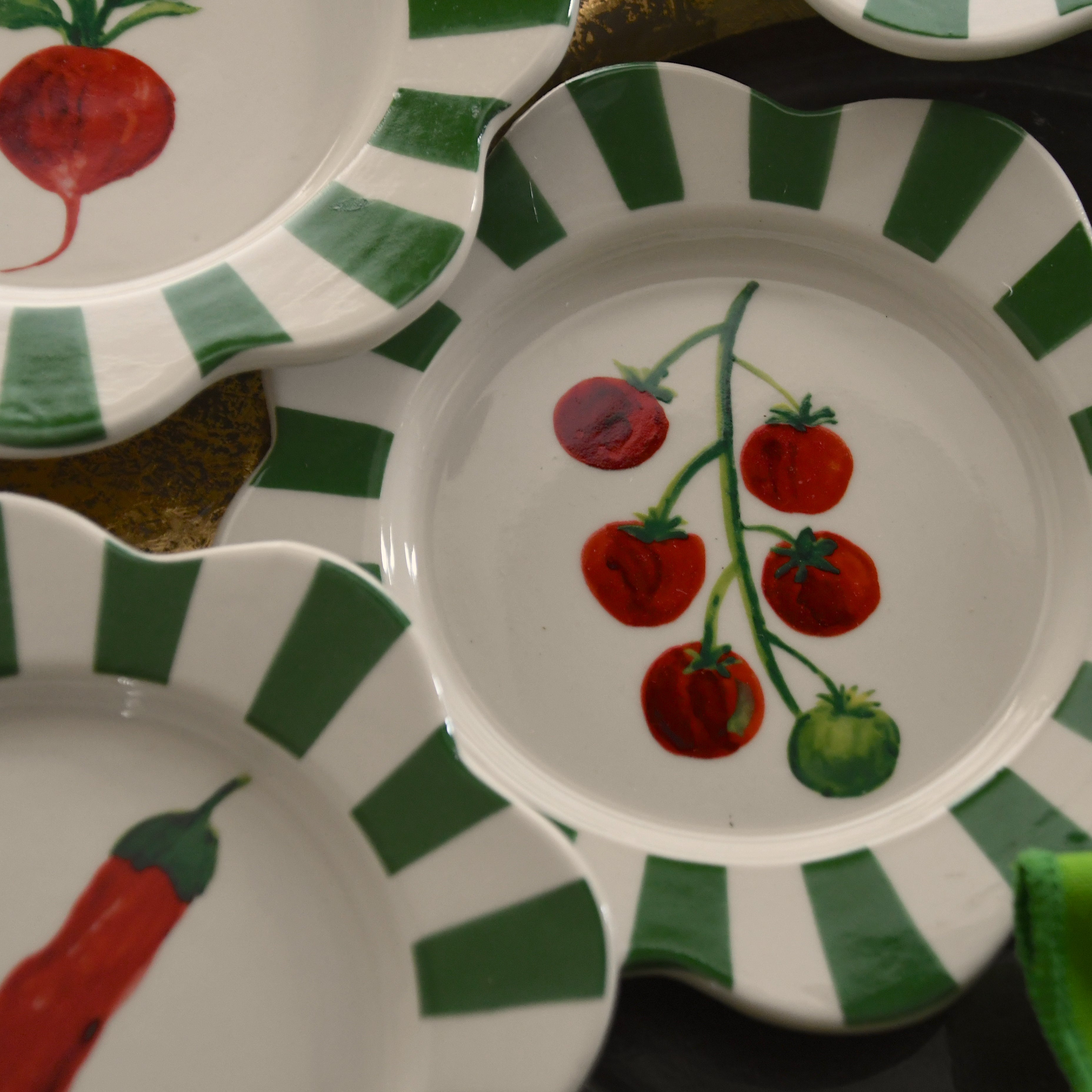 Set of ceramic plates with green stripes and colorful illustrations on a dark surface.