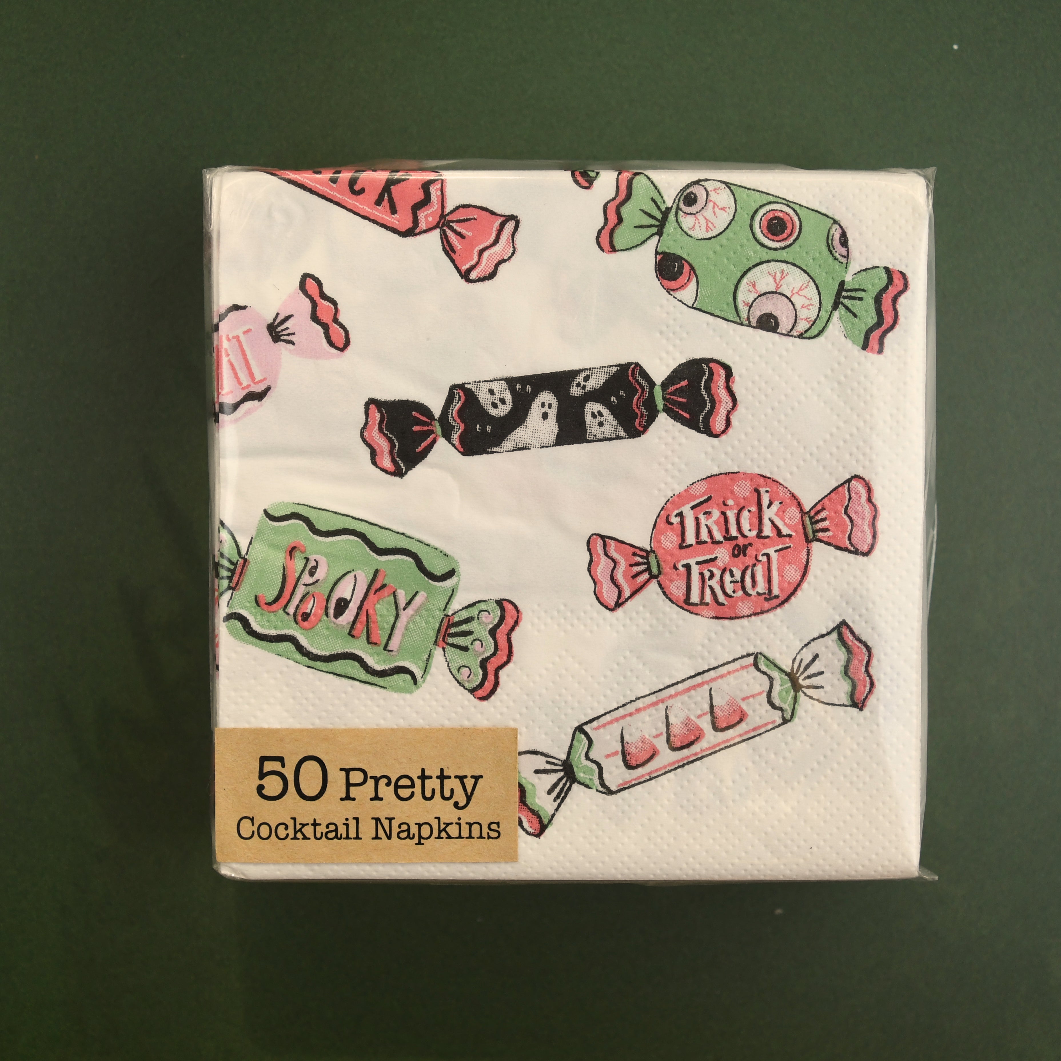 A pack of 50 Pretty Cocktail Napkins featuring a Halloween candy print, shown on a dark green background.