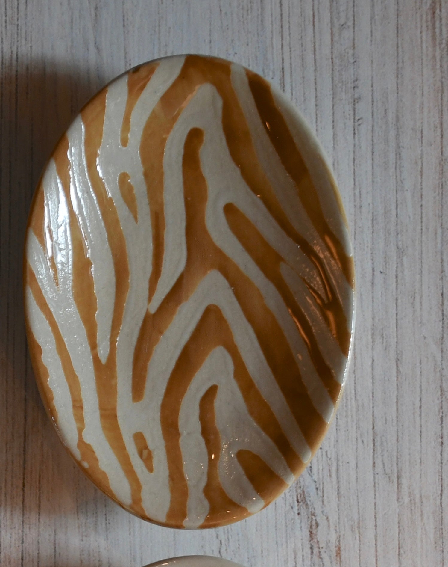 Round ceramic object with brown and white zebra-striped pattern on a wooden surface