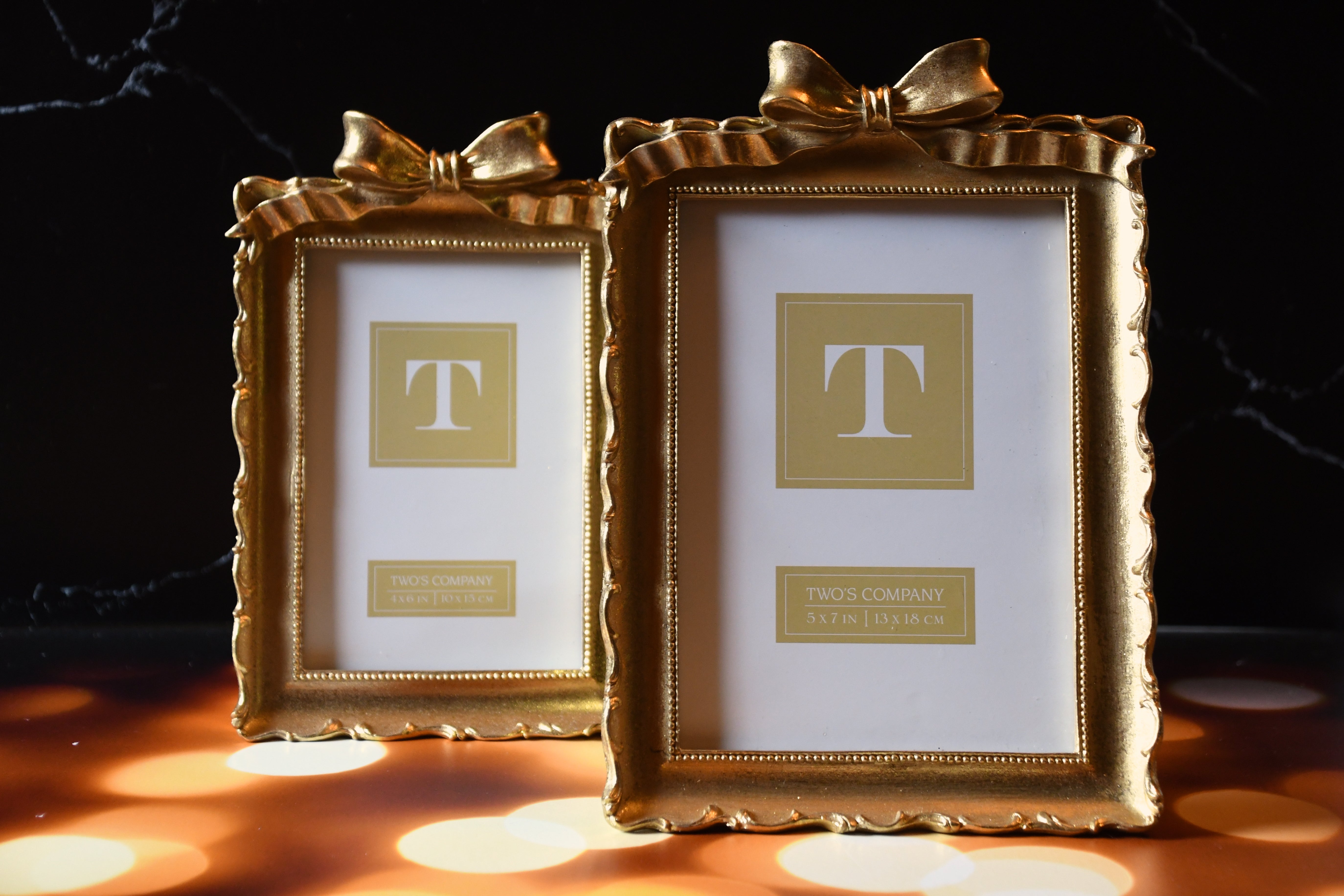 Two gold picture frames with decorative bows on a dark background