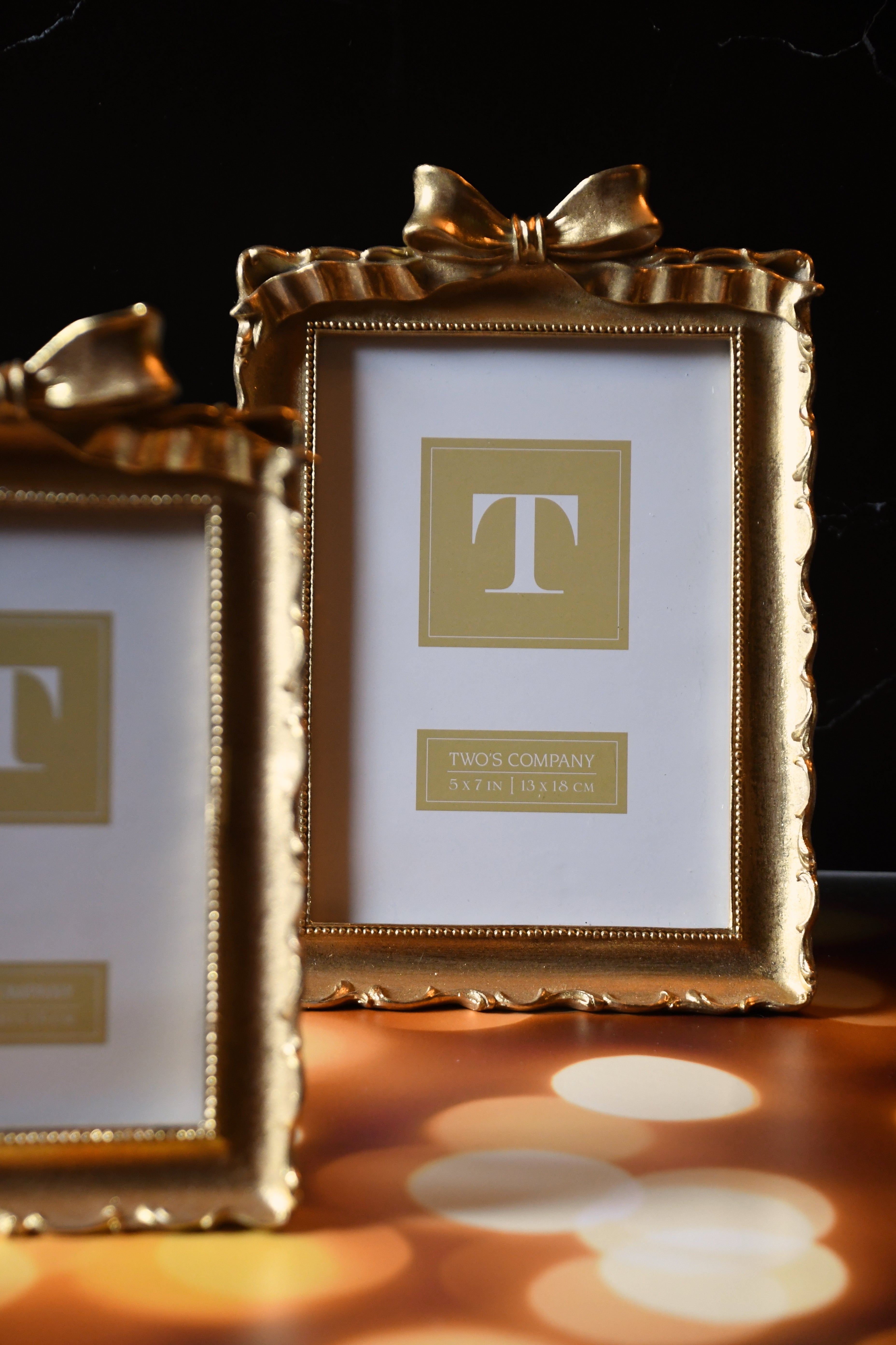 Two gold picture frames with a bow on a dark background