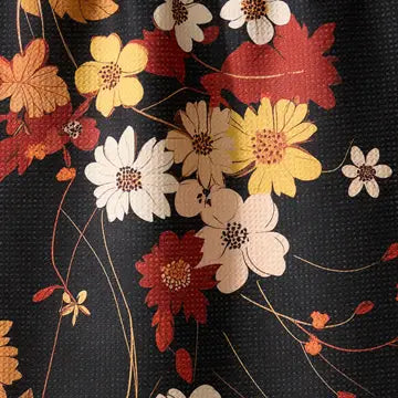 A close-up of a floral fabric pattern featuring yellow, white, and red flowers with brown centers on a black textured background.