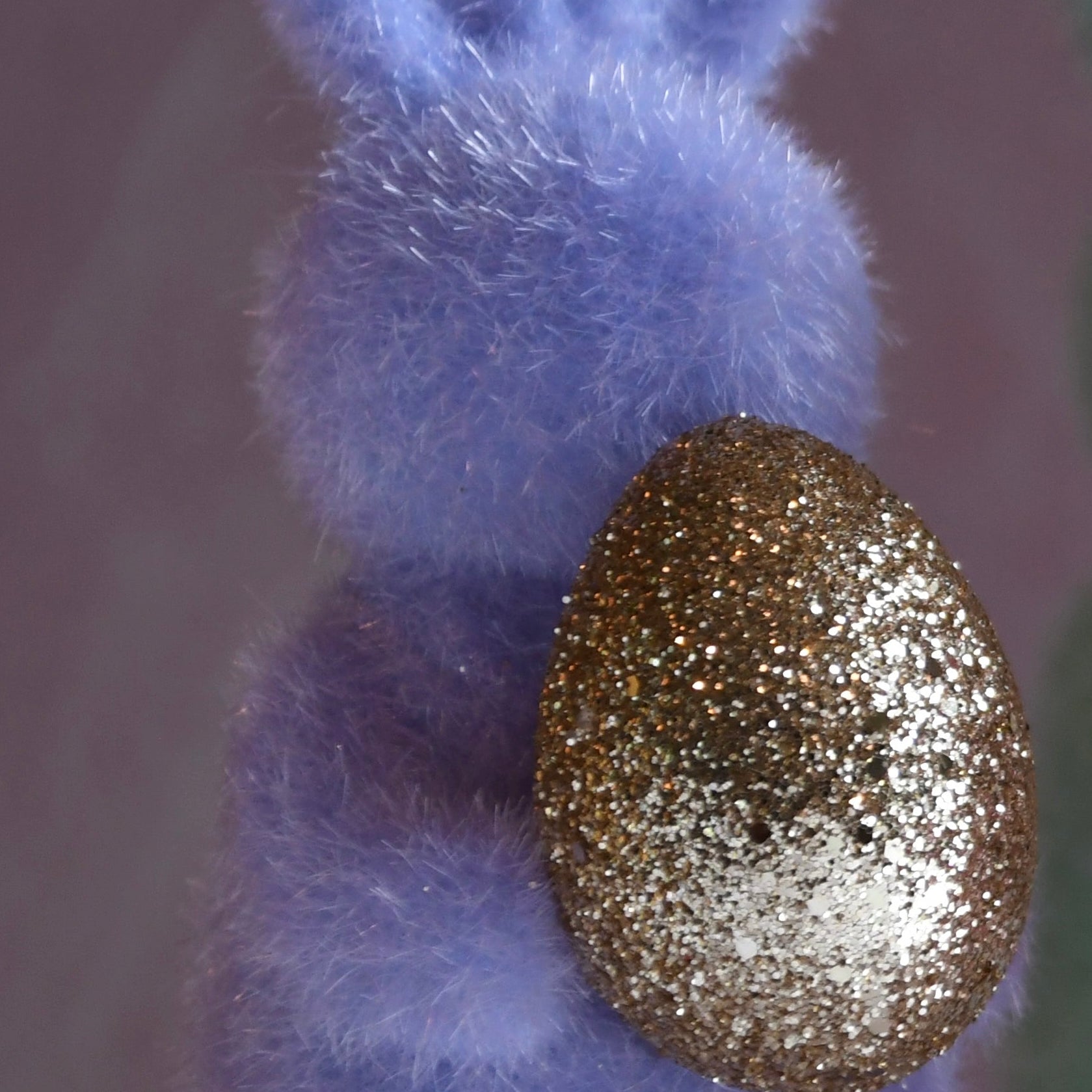 Purple bunny figurine holding a gold glittery egg against a gray background