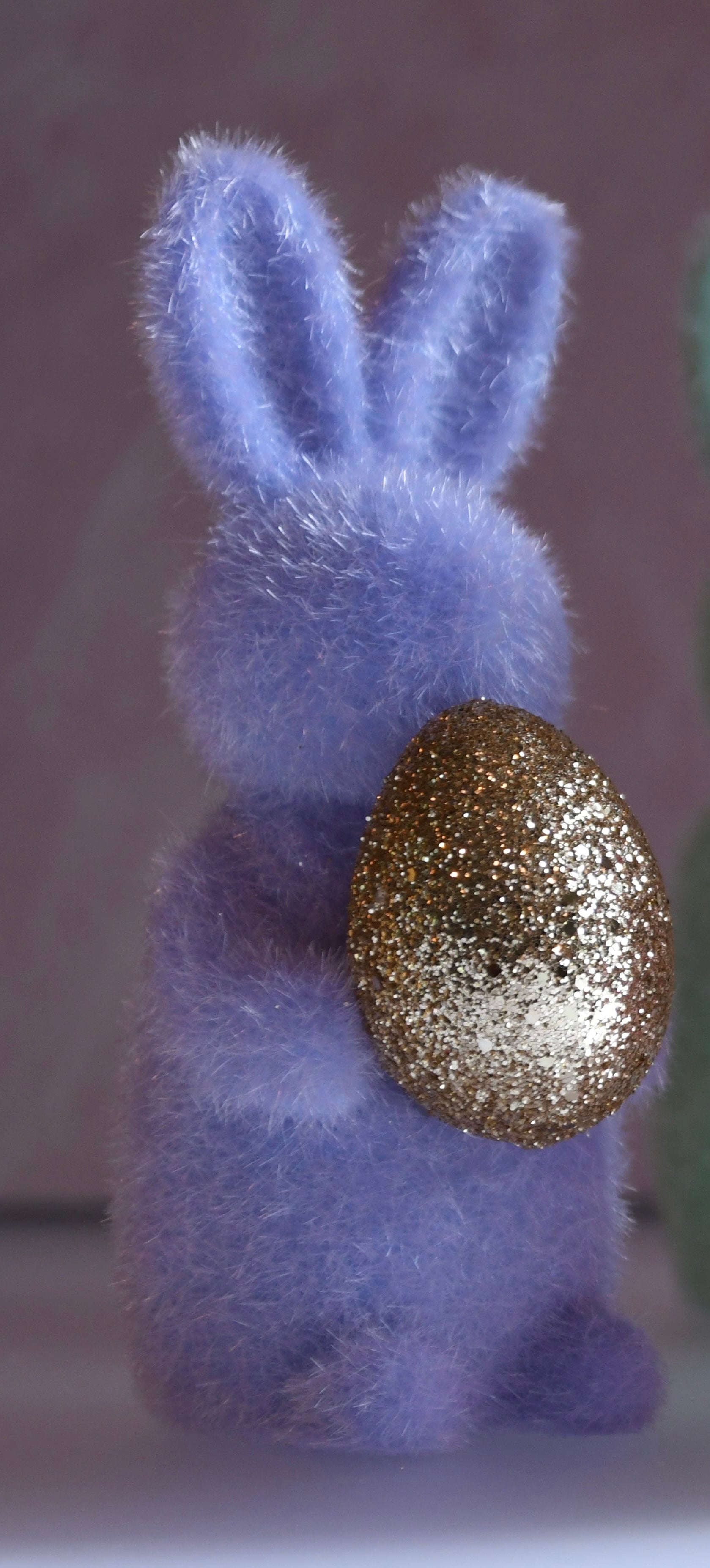 Purple bunny figurine holding a gold glittery egg against a gray background