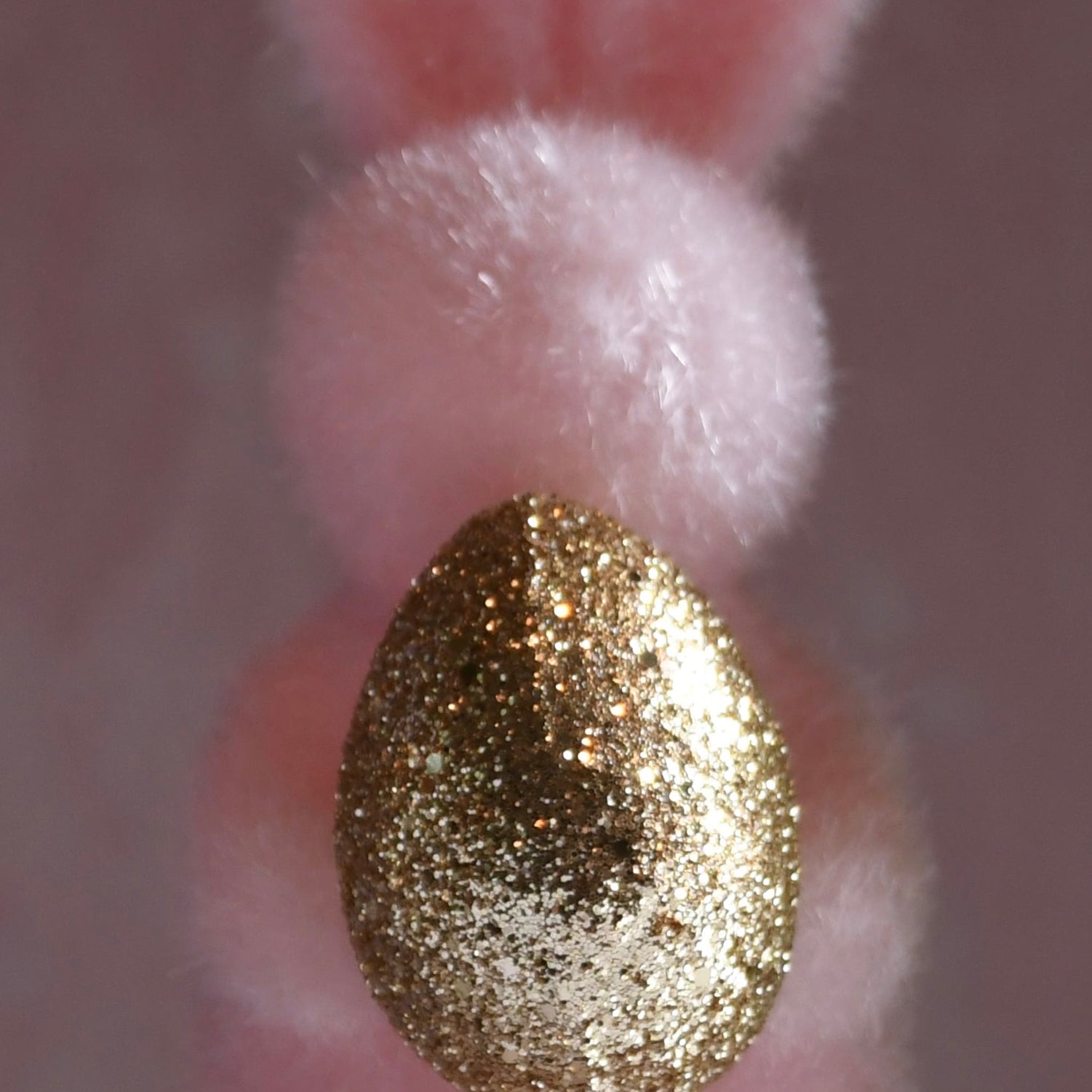 Pink plush bunny with a gold glittery egg on a blurred background