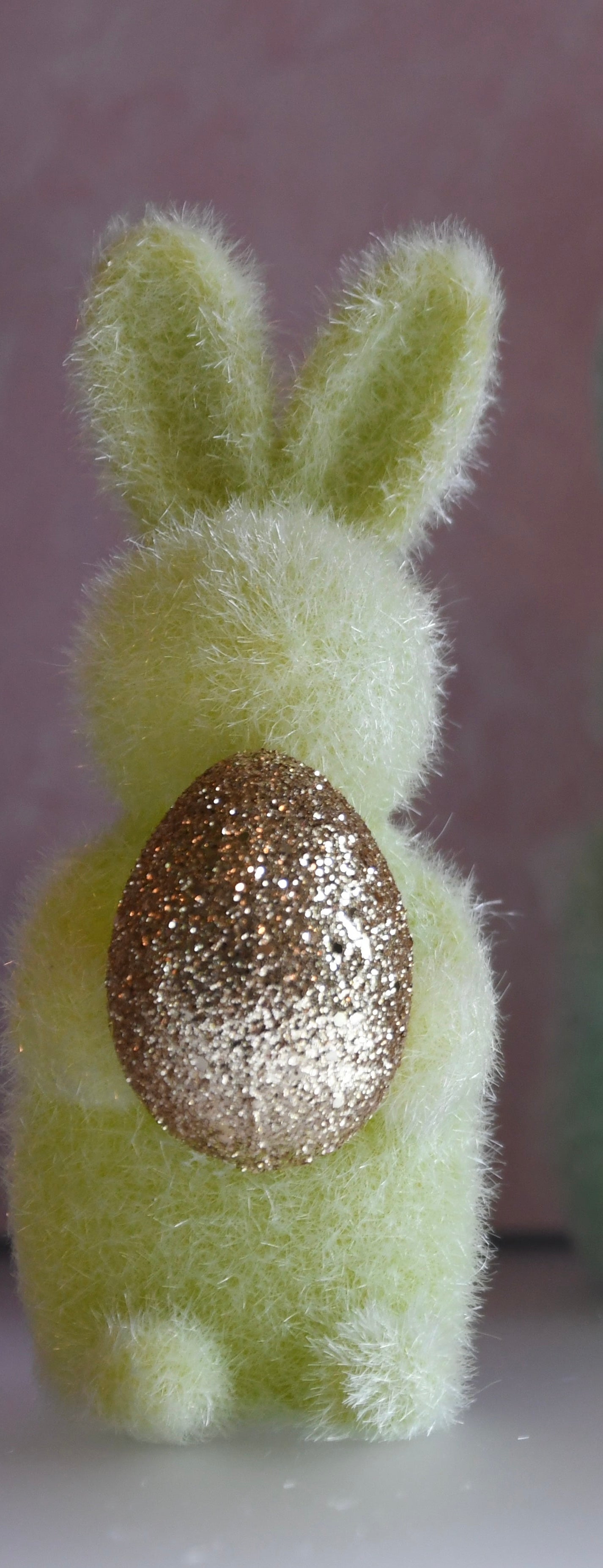 Green felt bunny with a glittery gold egg on a plain background
