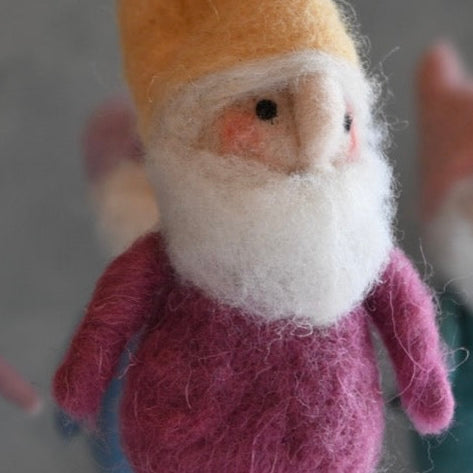Felted gnome figurine with a yellow hat and pink outfit on a neutral background