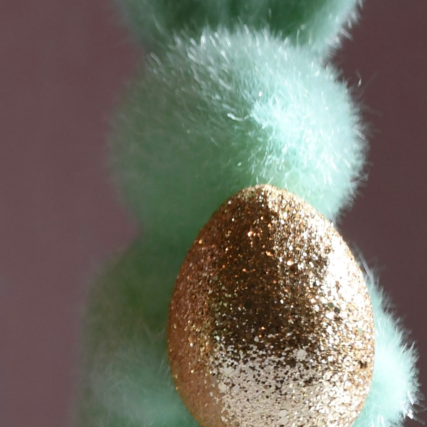 Green felt bunny with a gold glittery egg on a plain background