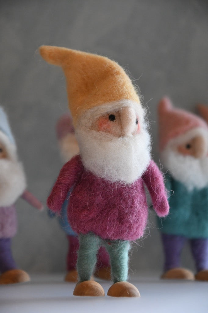 Felted gnome figurine with a yellow hat and pink outfit on a gray background