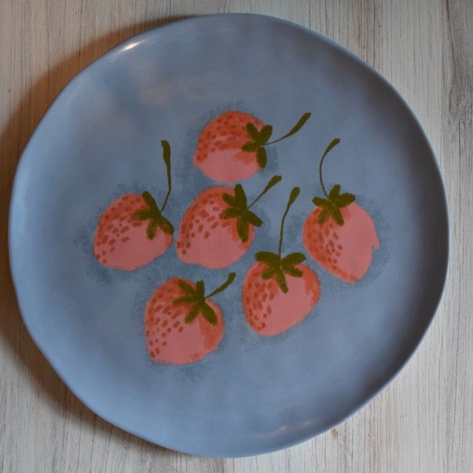 Blue plate with pink strawberry design on a wooden surface