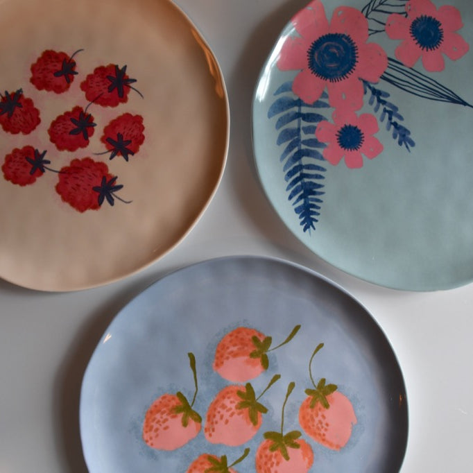 Three decorative plates with floral and strawberry designs on a white surface