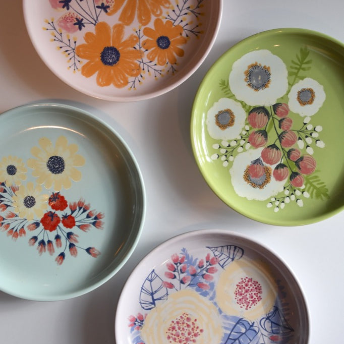 Four decorative plates with floral designs on a light gray background