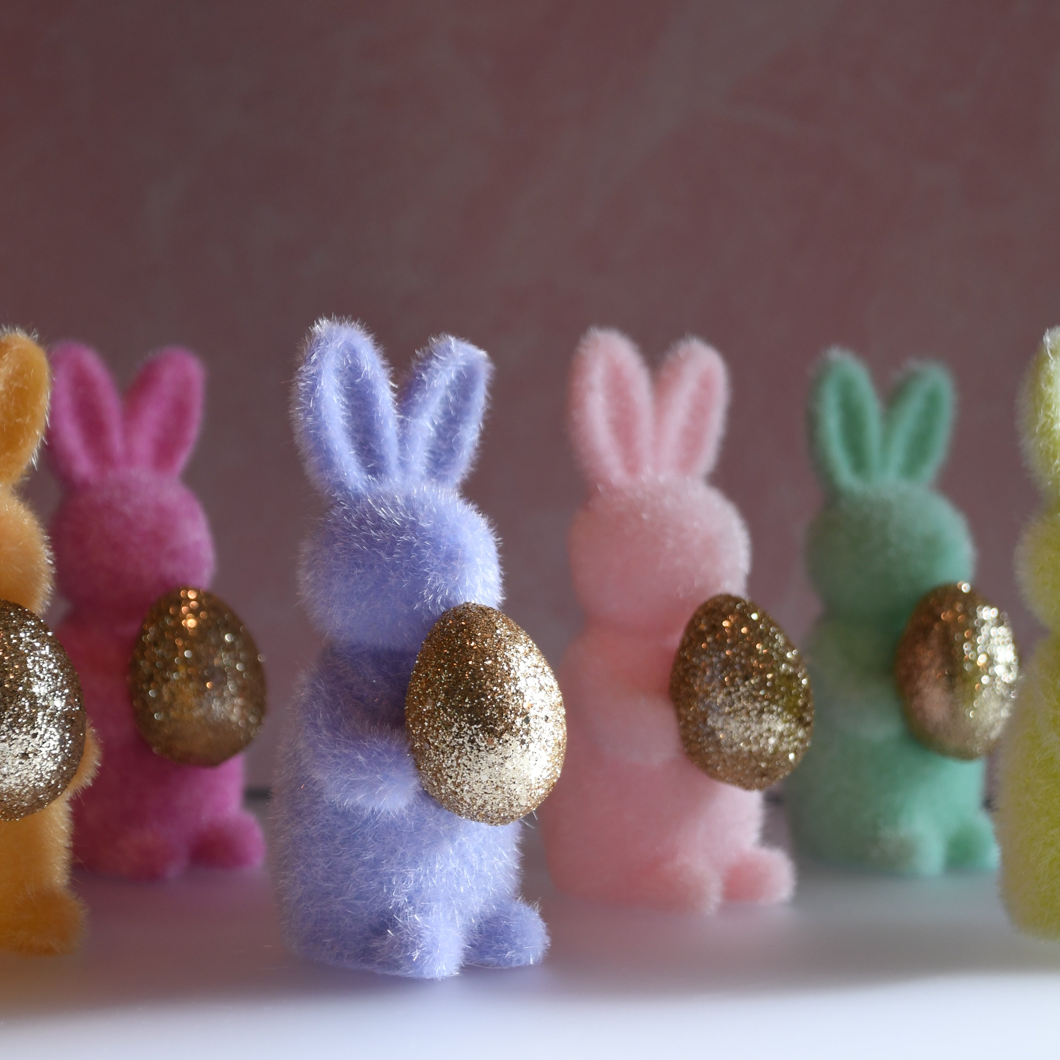 Colorful foam bunny figurines with glittery eggs on a pink background