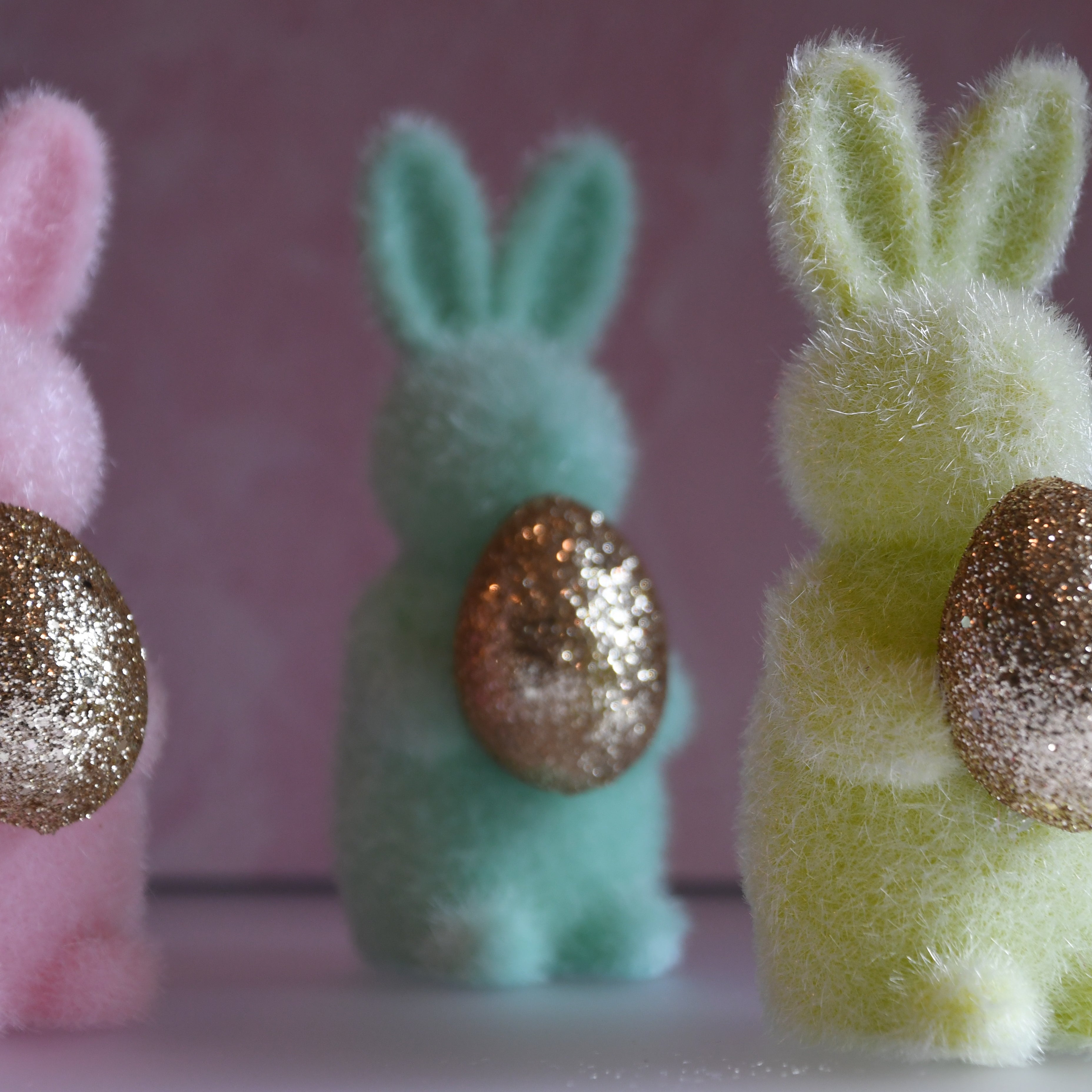 Three colorful foam bunny figures with glittery eggs on a pink background