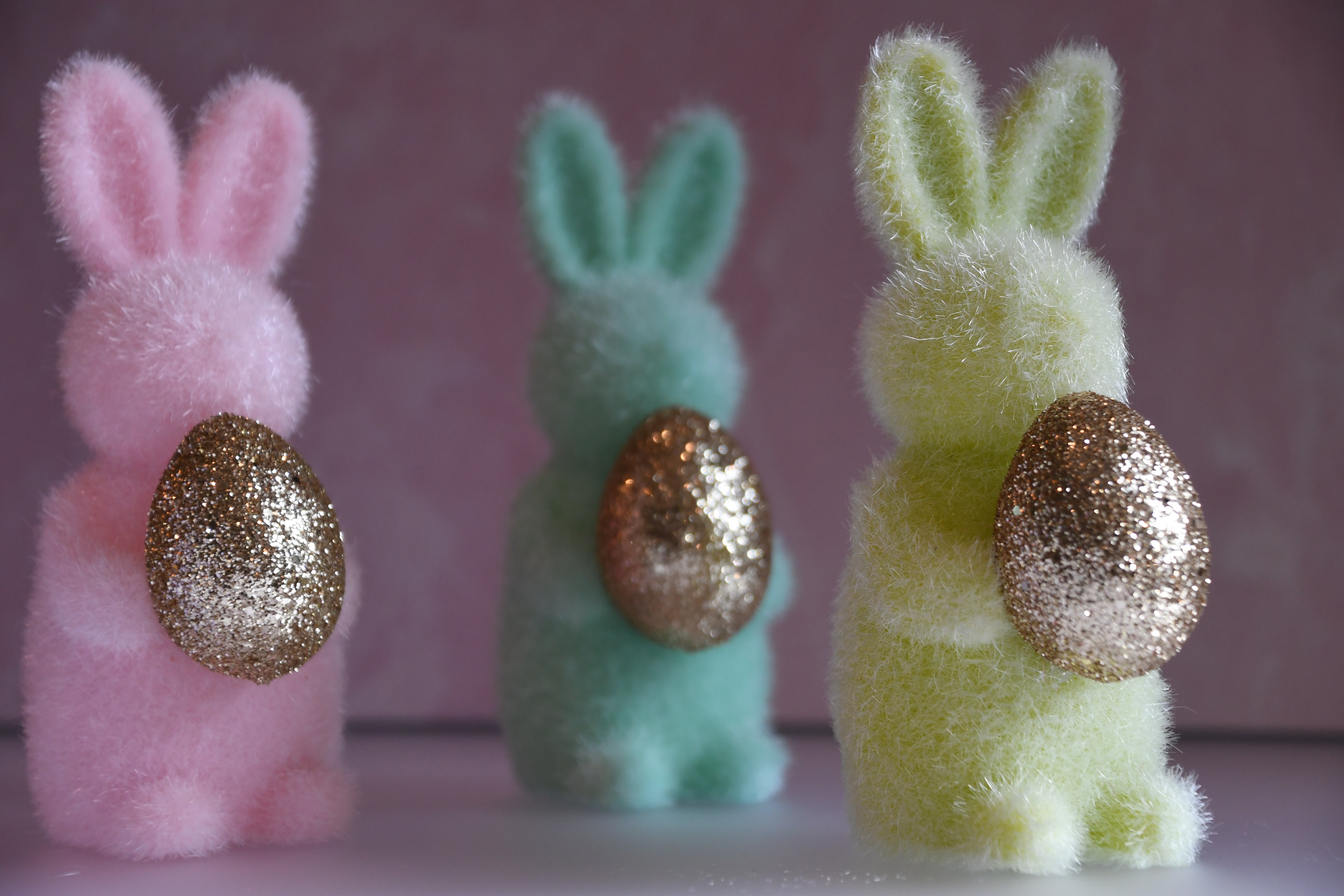 Three colorful foam bunny figures with glittery eggs on a pink background