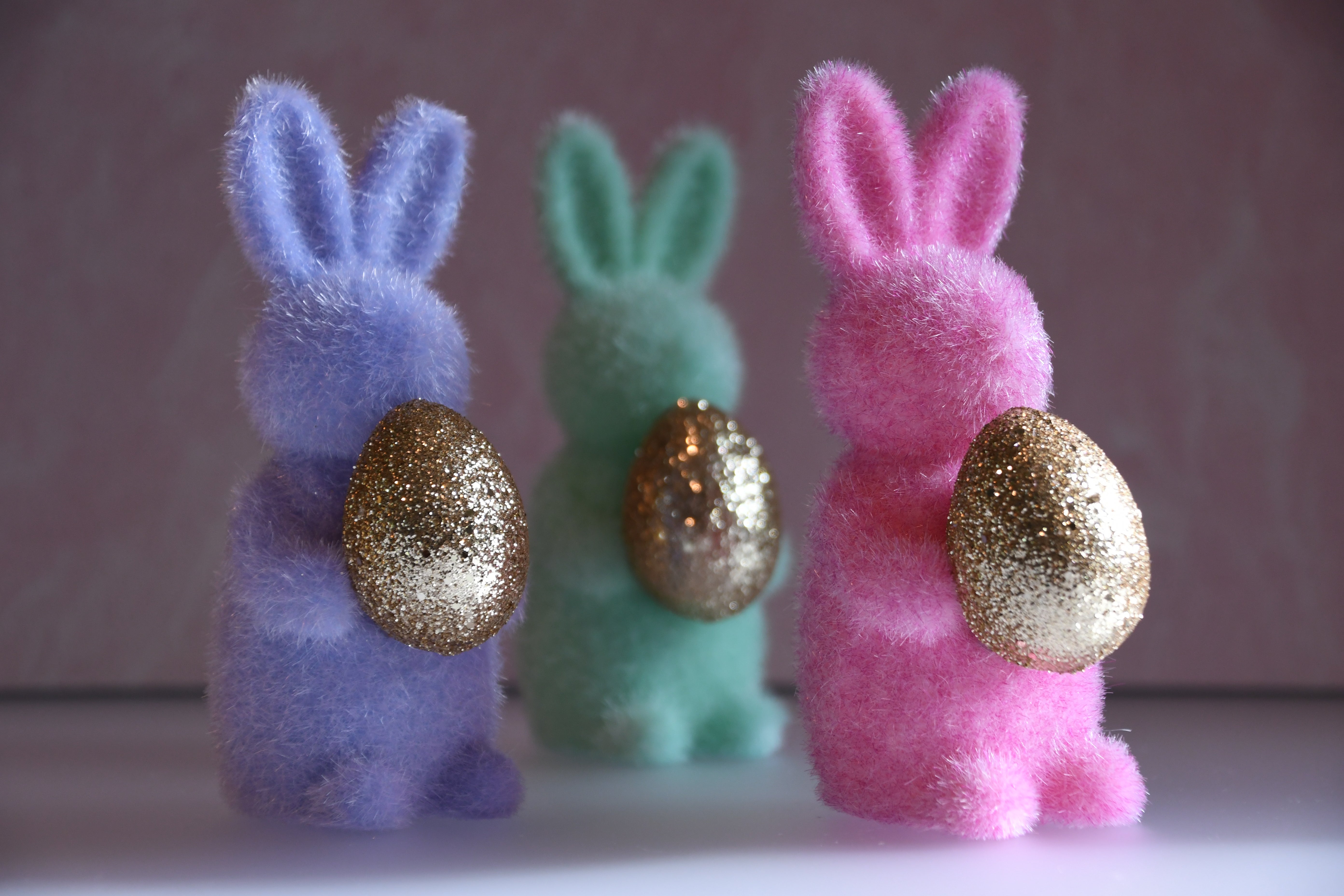 Three colorful bunny figurines with glittery eggs on a plain background