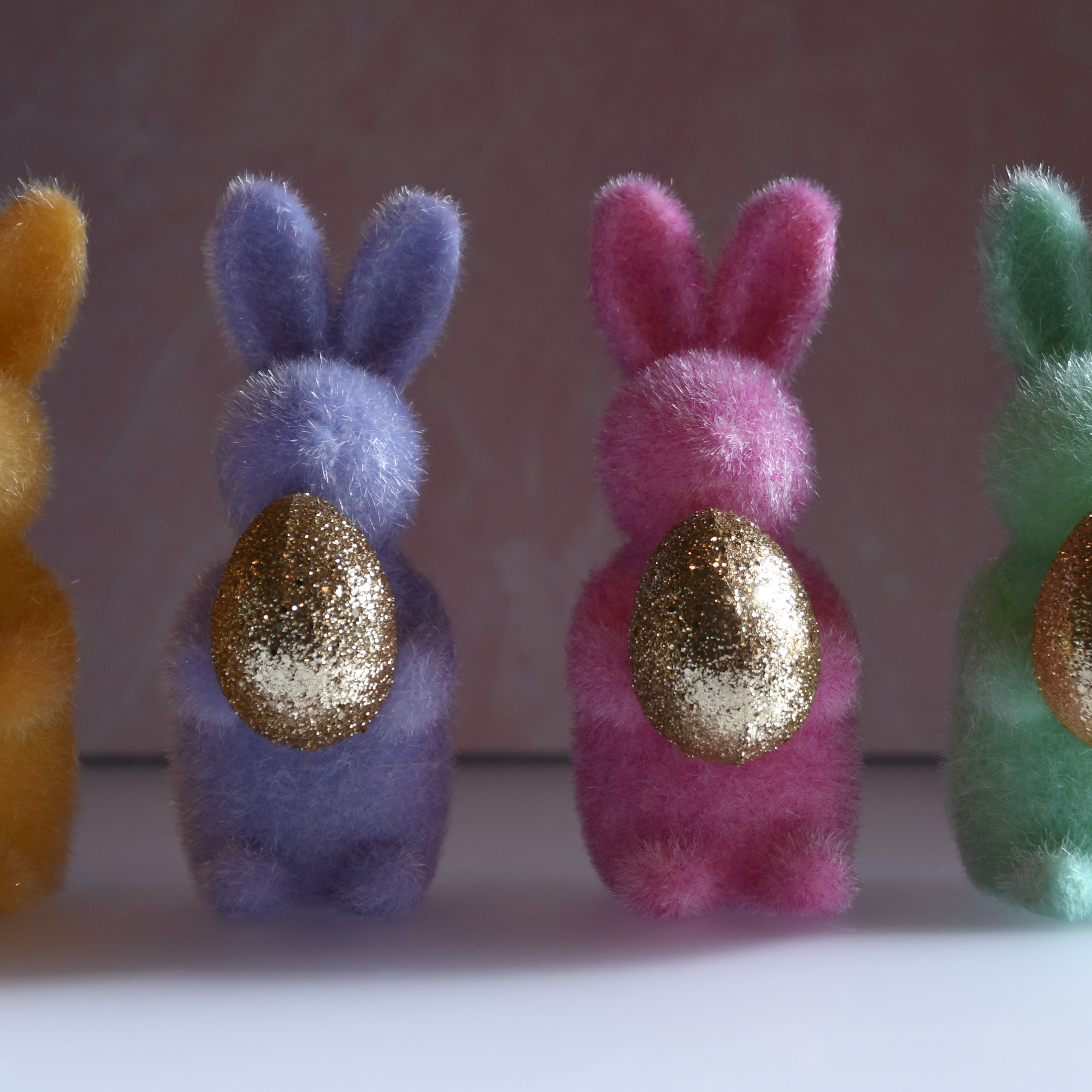 Four colorful bunny figurines with gold eggs on a plain background