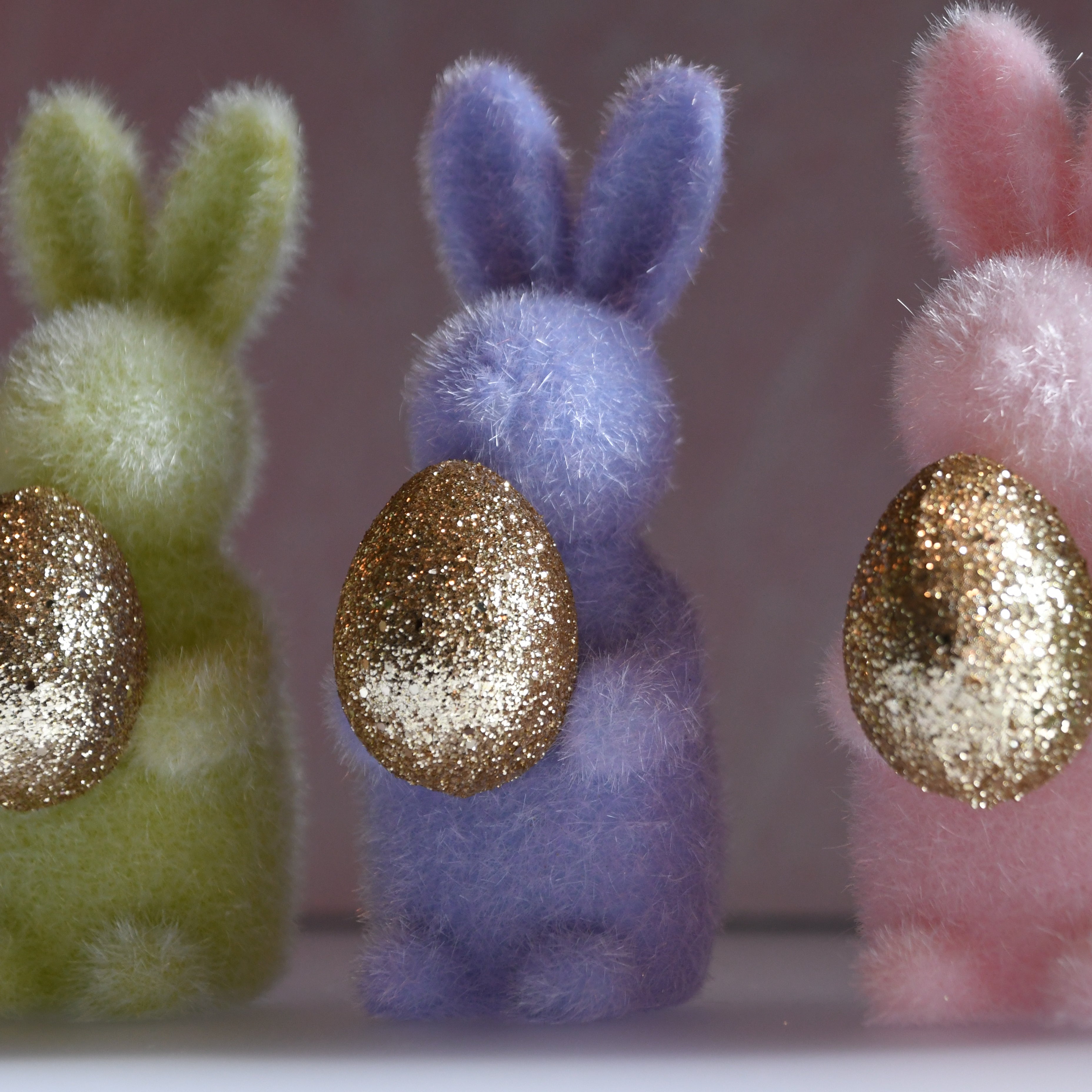 Three fluffy bunny toys with glittery golden eggs on a blurred background