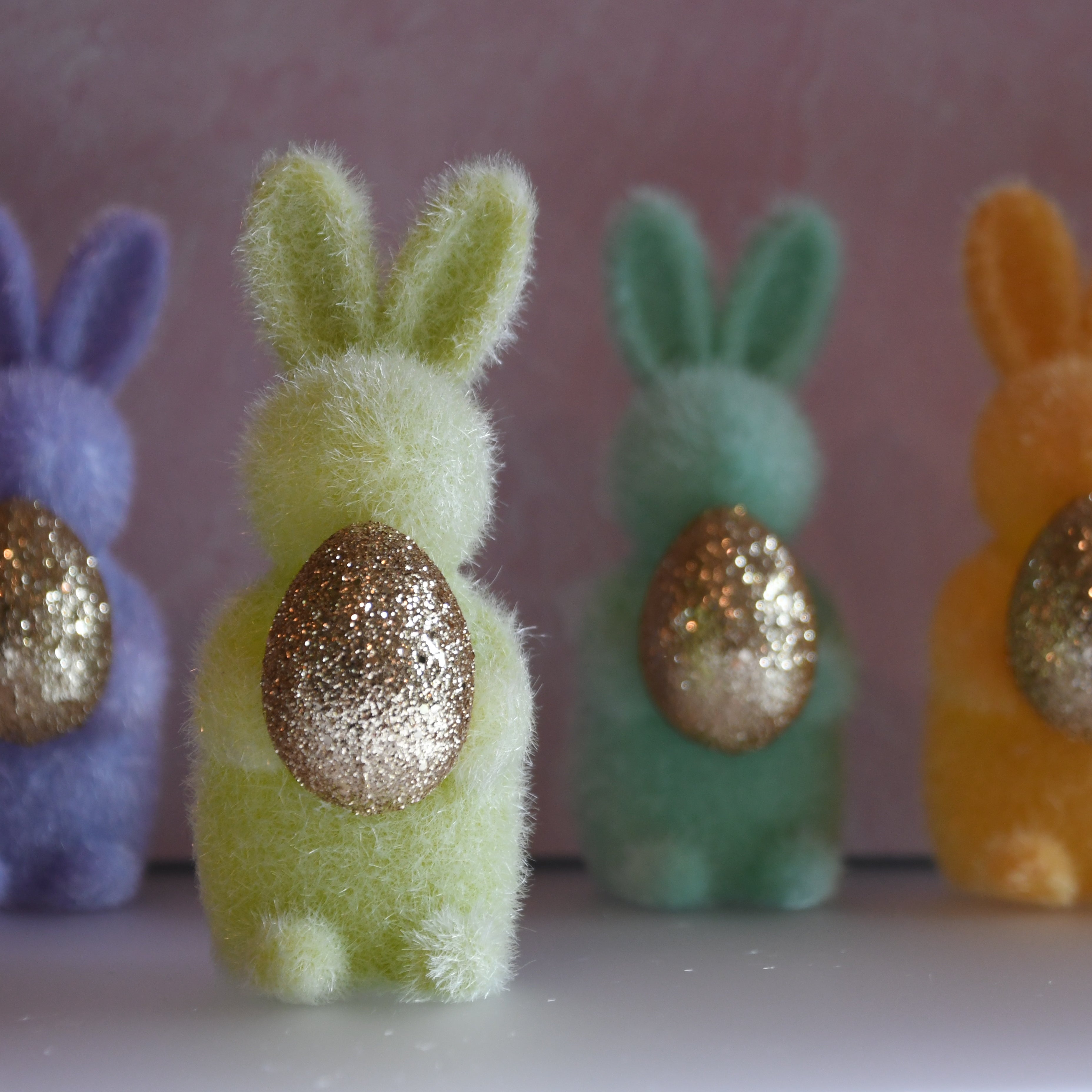 Four colorful bunny figurines with glittery eggs on a pink background