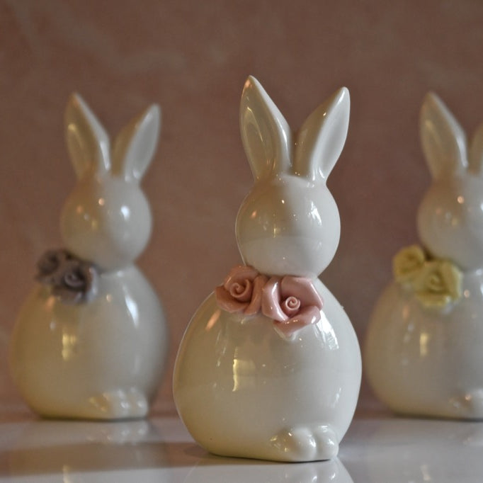 Three ceramic rabbit figurines with floral decorations on a reflective surface.