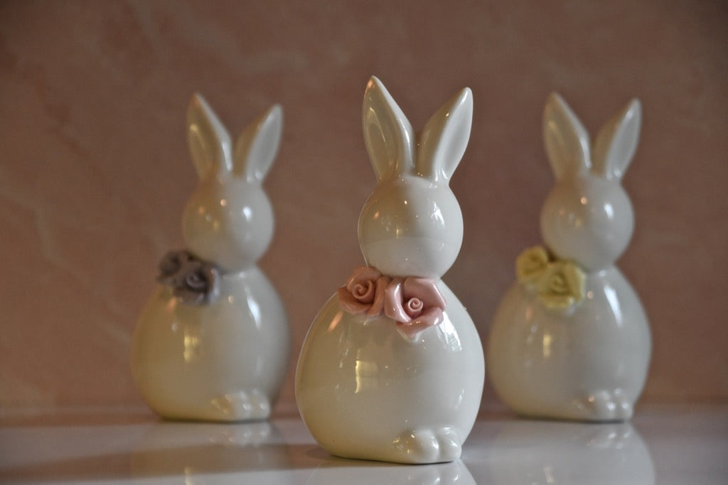 Three ceramic rabbit figurines with floral decorations on a reflective surface.