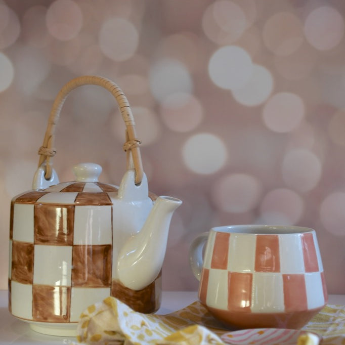 Ceramic teapot and mug with checkered pattern on a blurred bokeh background