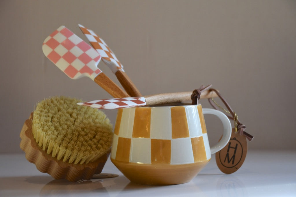 Ceramic mug with checkered pattern, scrub brush, and spatula on a neutral background