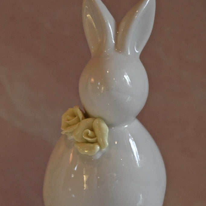 White ceramic bunny figurine with a yellow rose on a pink background