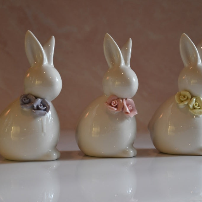 Three ceramic rabbit figurines with decorative flowers on a reflective surface.