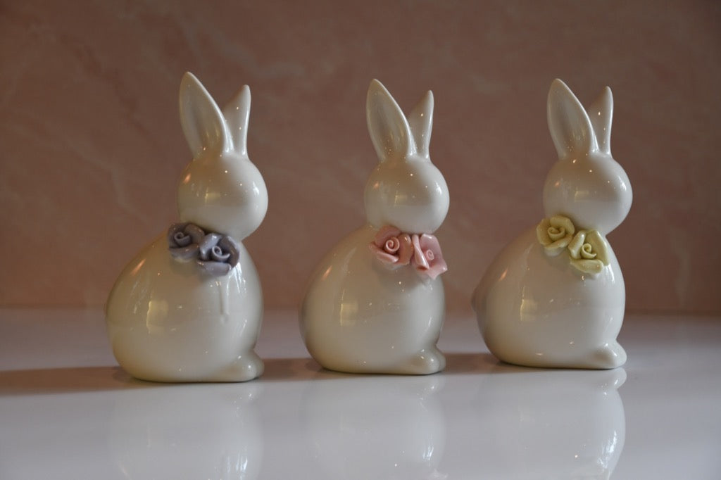 Three ceramic rabbit figurines with decorative flowers on a reflective surface.