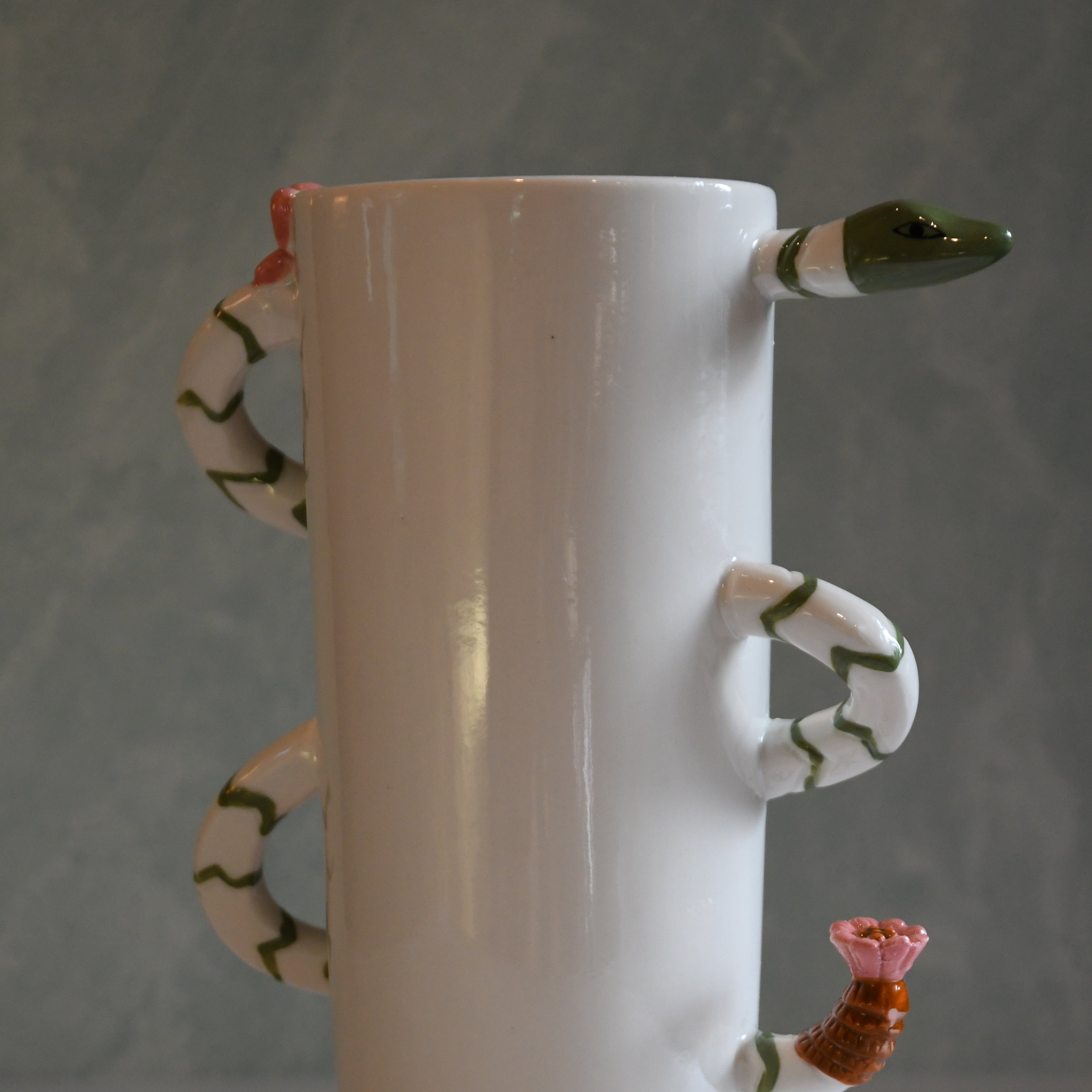 White ceramic vase with snake handles and a flower on a gray background