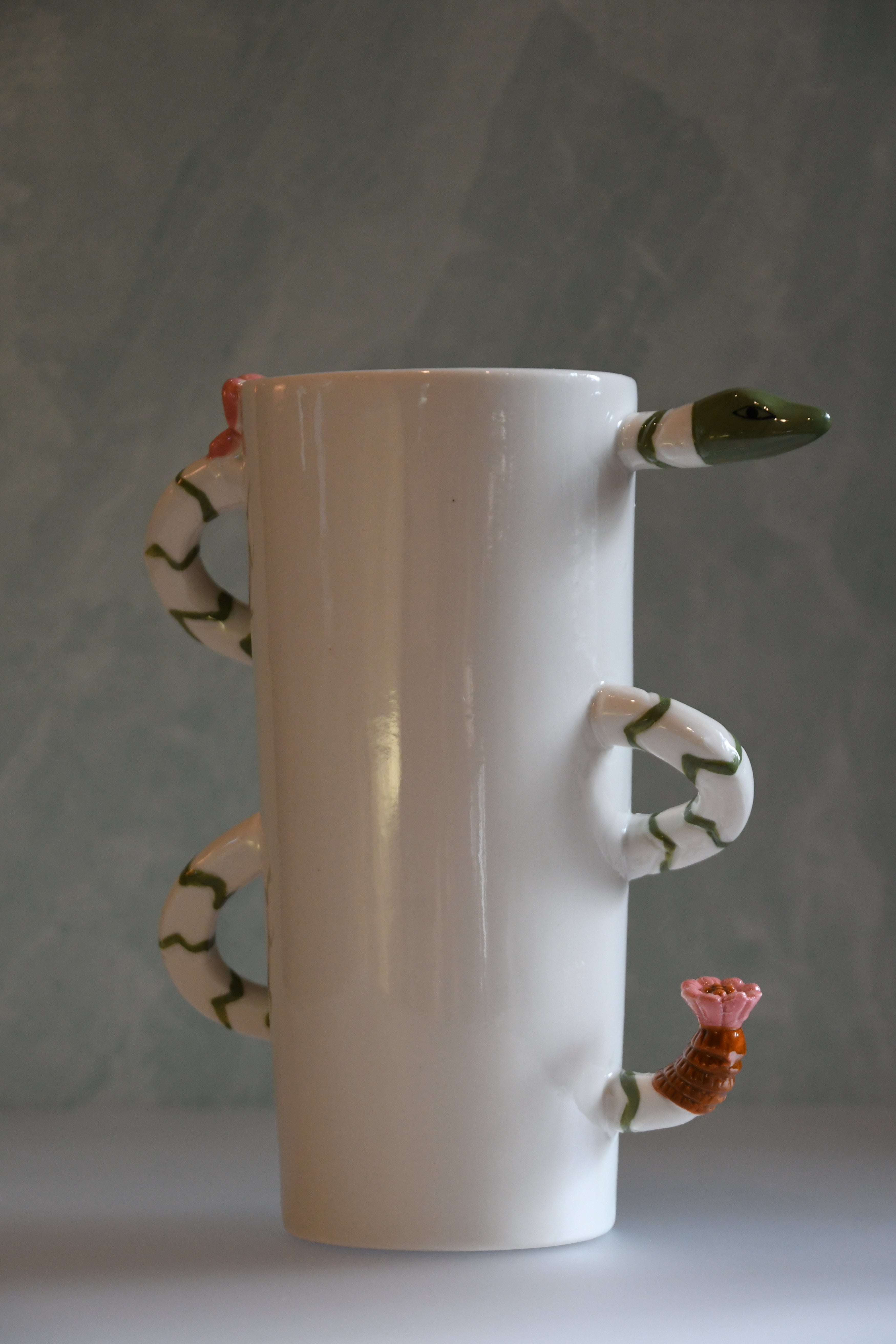 White ceramic vase with snake handles and a flower on a gray background