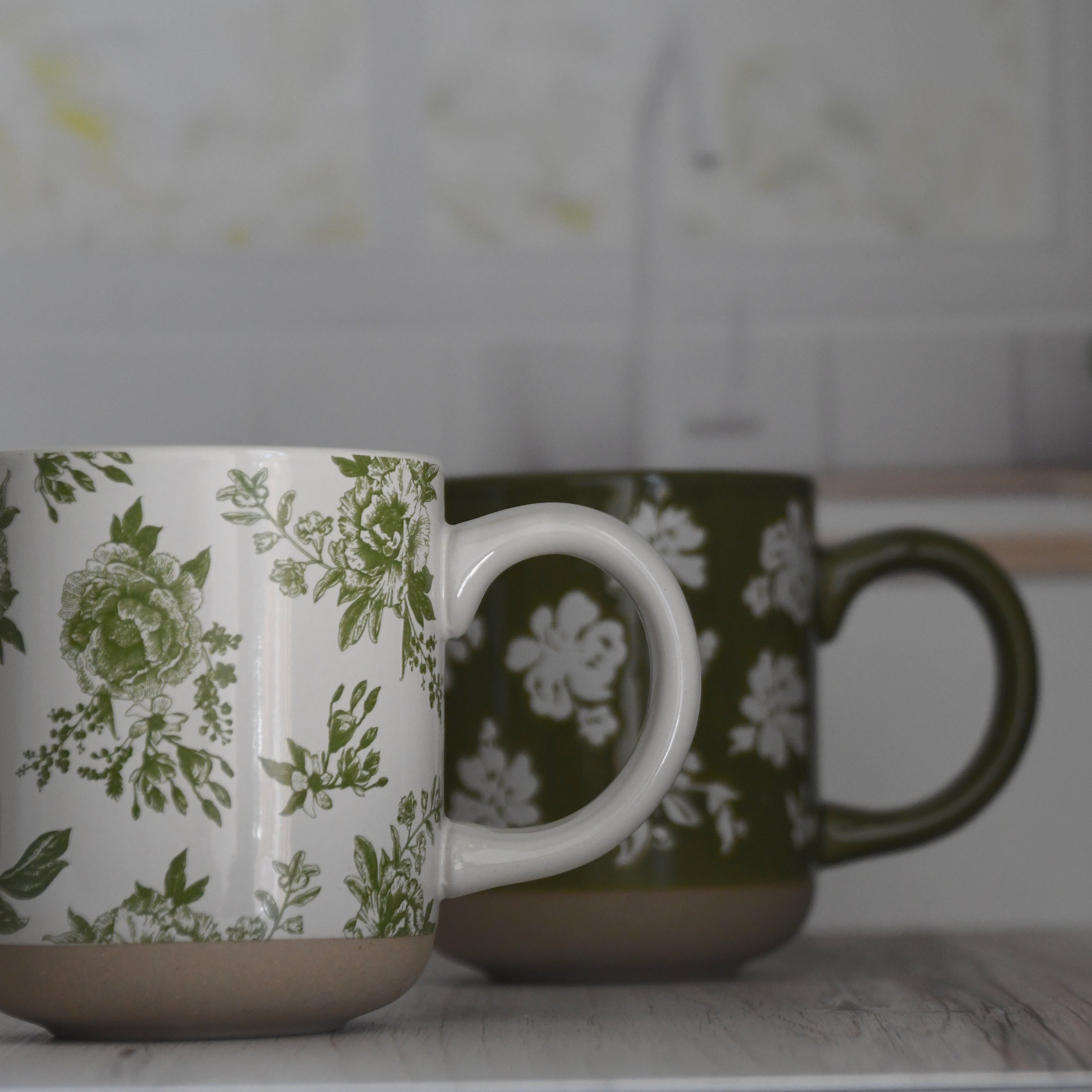 Two ceramic mugs with floral patterns on a kitchen counter.