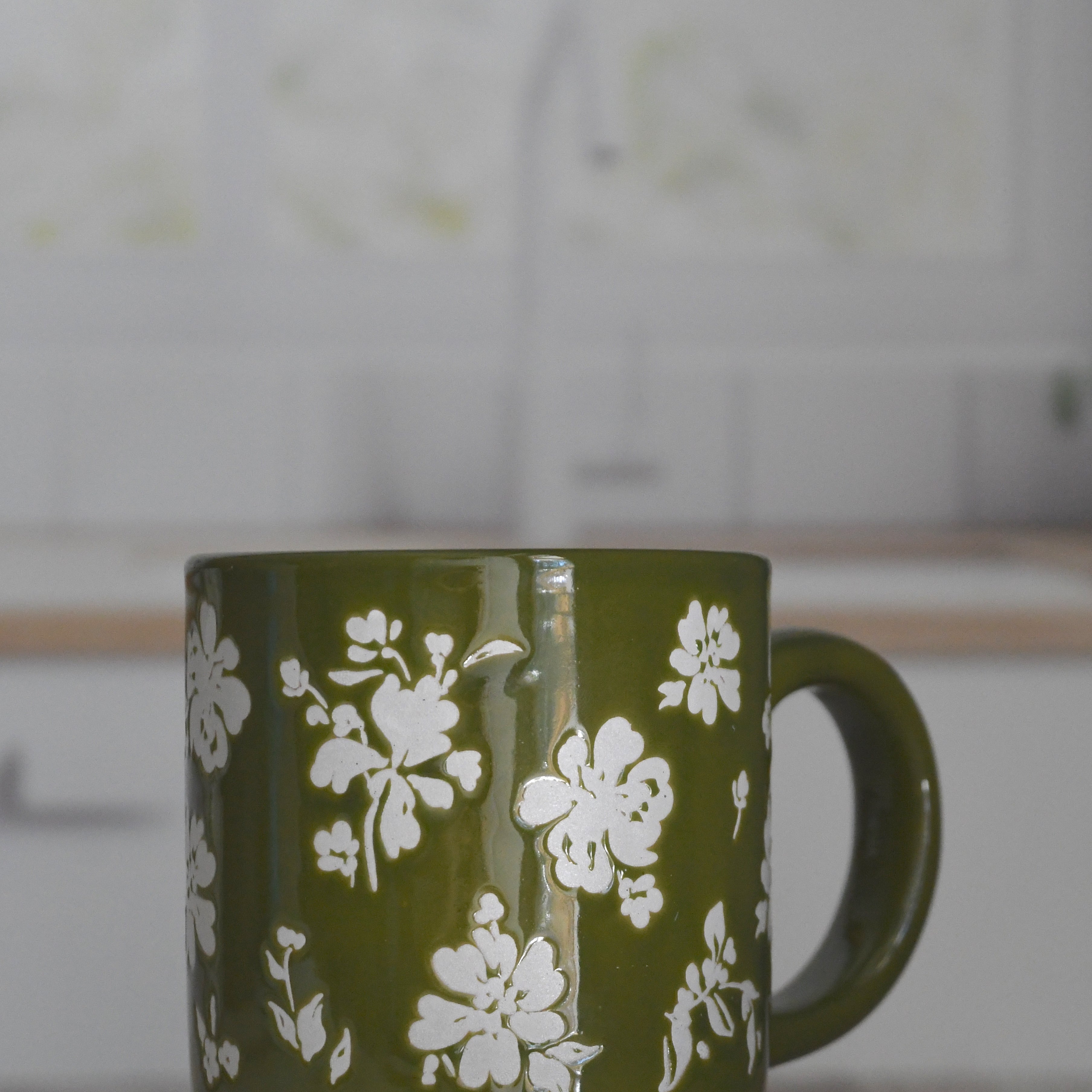 Green mug with white floral pattern on a wooden surface