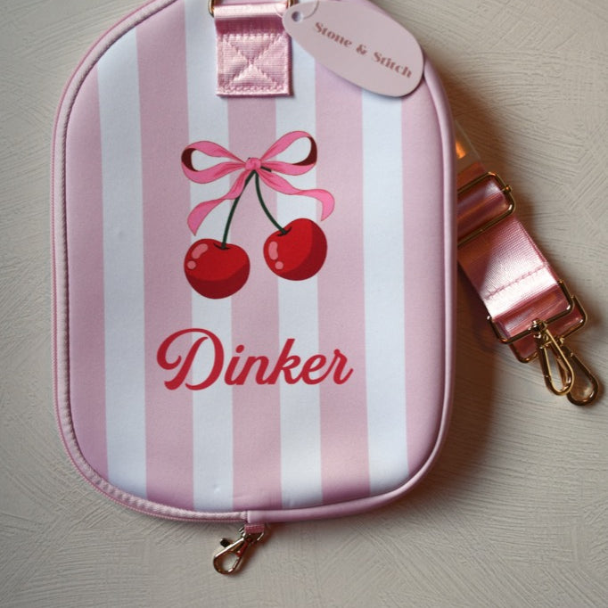 Pink and white striped pouch with cherry design and 'Dinker' text on a light gray background