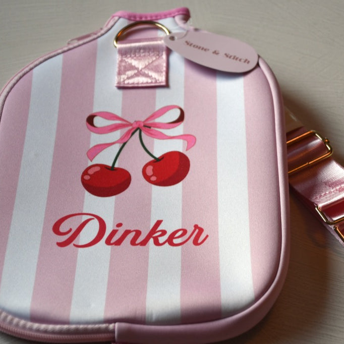 Pink and white striped pouch with cherry design and 'Dinker' branding on a light gray background