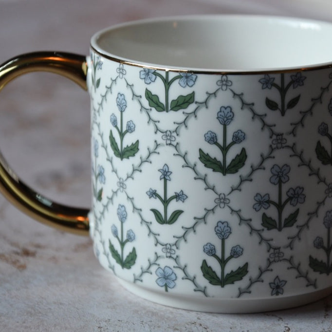 White mug with floral pattern and gold handle on a textured surface