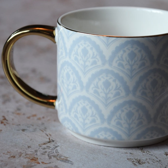 Ceramic mug with gold handle and blue geometric pattern on a textured surface
