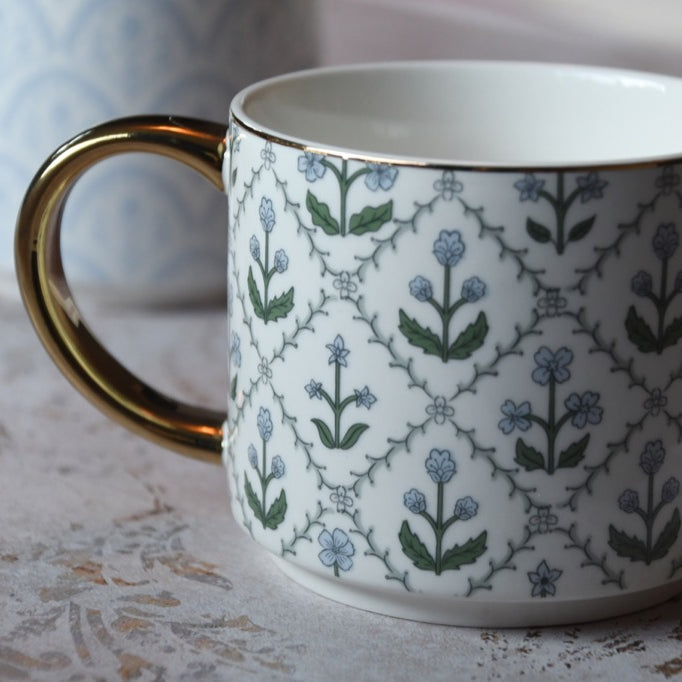White mug with floral pattern and gold handle on a textured surface