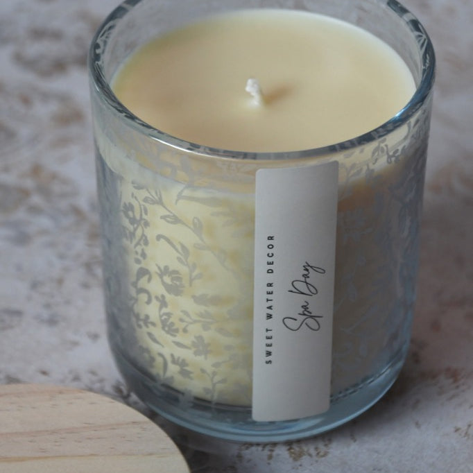 Candle in a glass jar with a decorative label on a textured surface