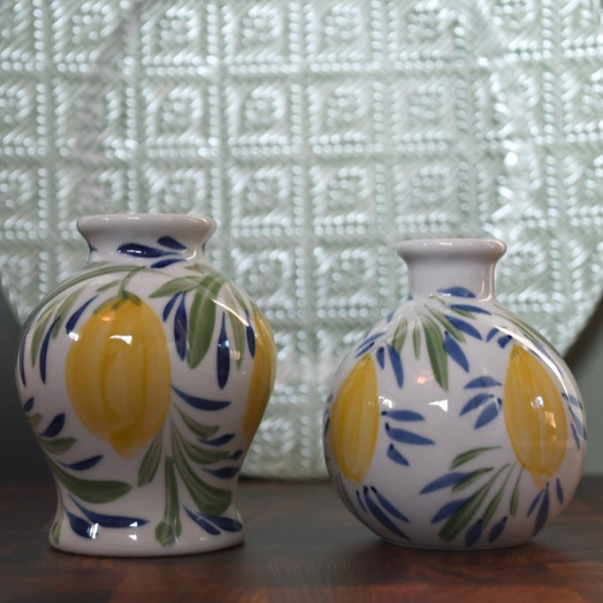 Two ceramic vases with lemon design on a wooden surface with a textured wall in the background.