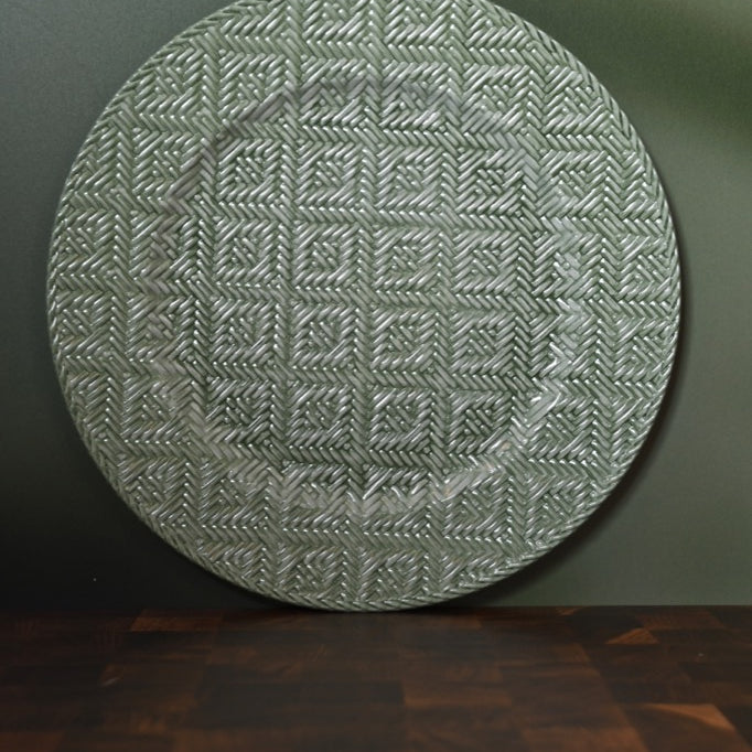 Round textured green rug on a dark surface with a green wall background
