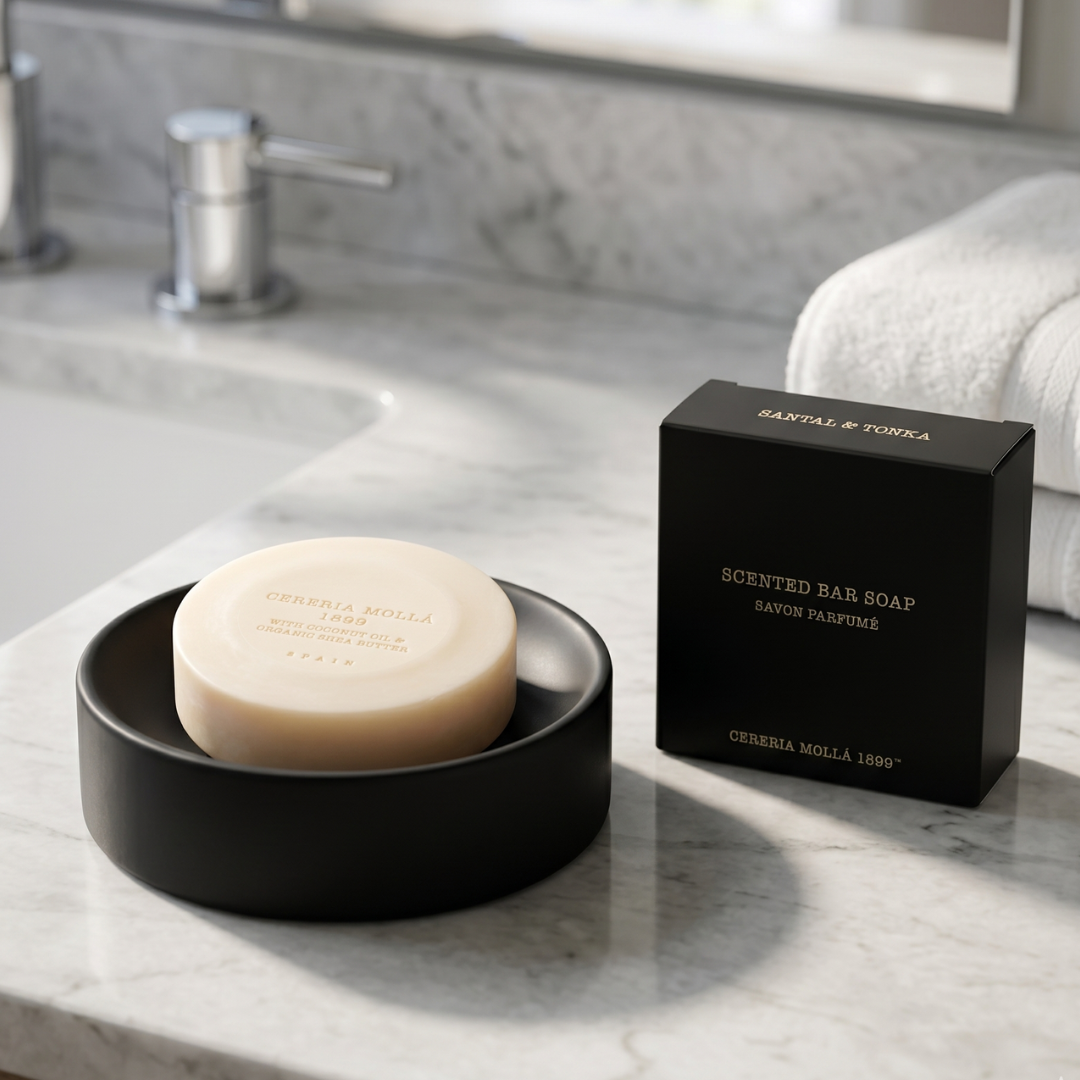 Scented bar soap in a black dish with its packaging on a marble countertop.