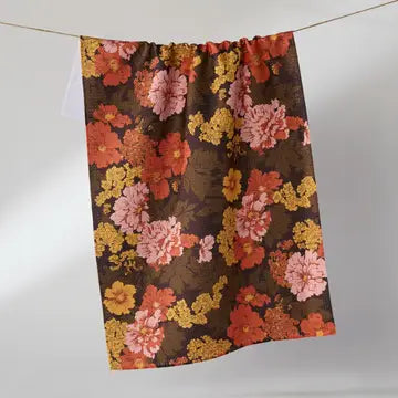 A gathered curtain panel with a dense floral pattern in pink, orange, yellow, and red on a dark brown background, hanging from a thin cord against a light gray wall.