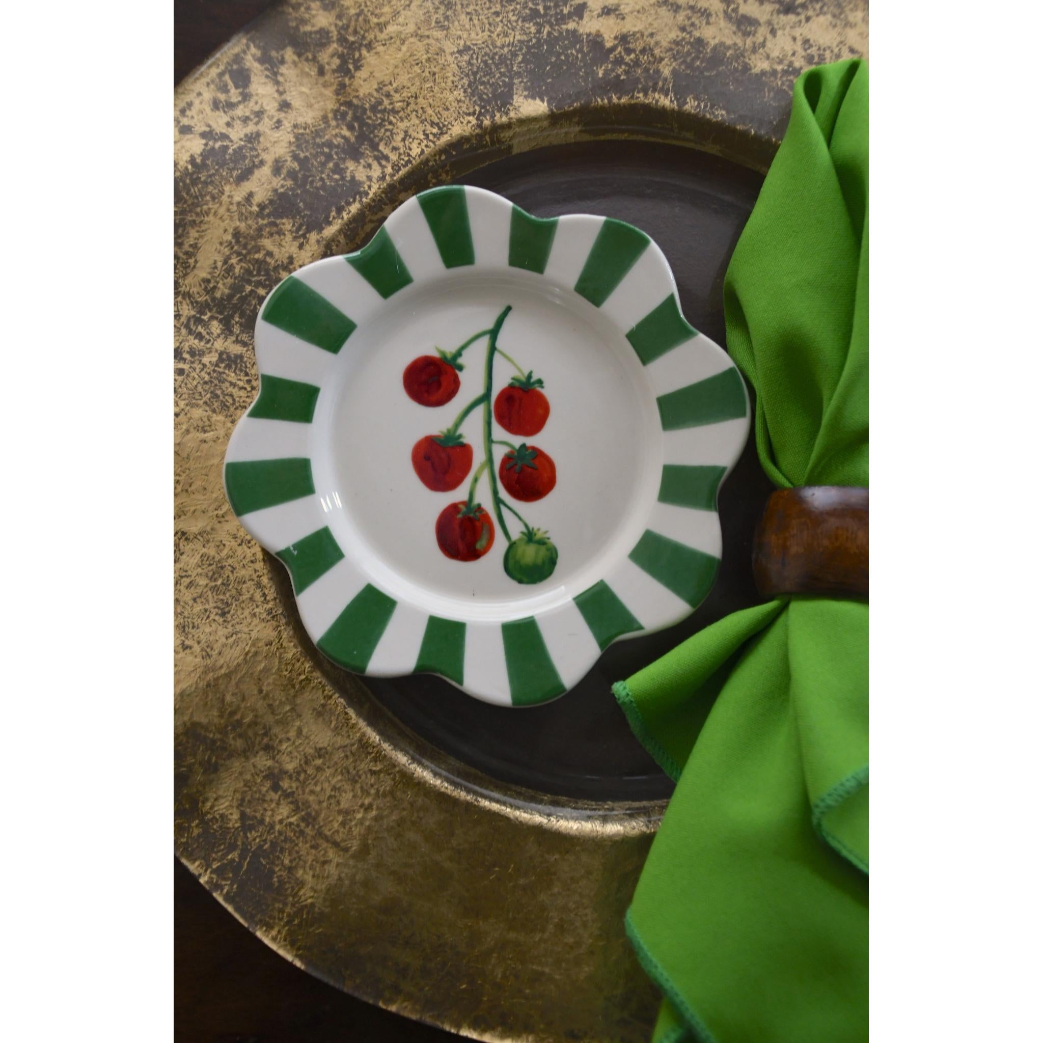 Decorative plate with cherry design on a green and white striped border, placed on a textured surface with a green napkin.