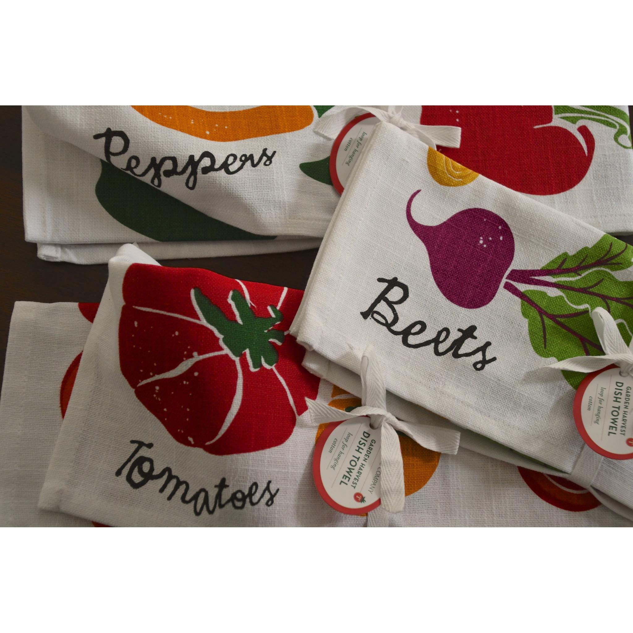 Set of kitchen towels with vegetable designs and labels on a wooden surface.